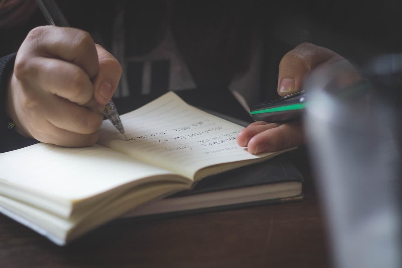 A student studying with a laptop and notebook, drafting an assignment