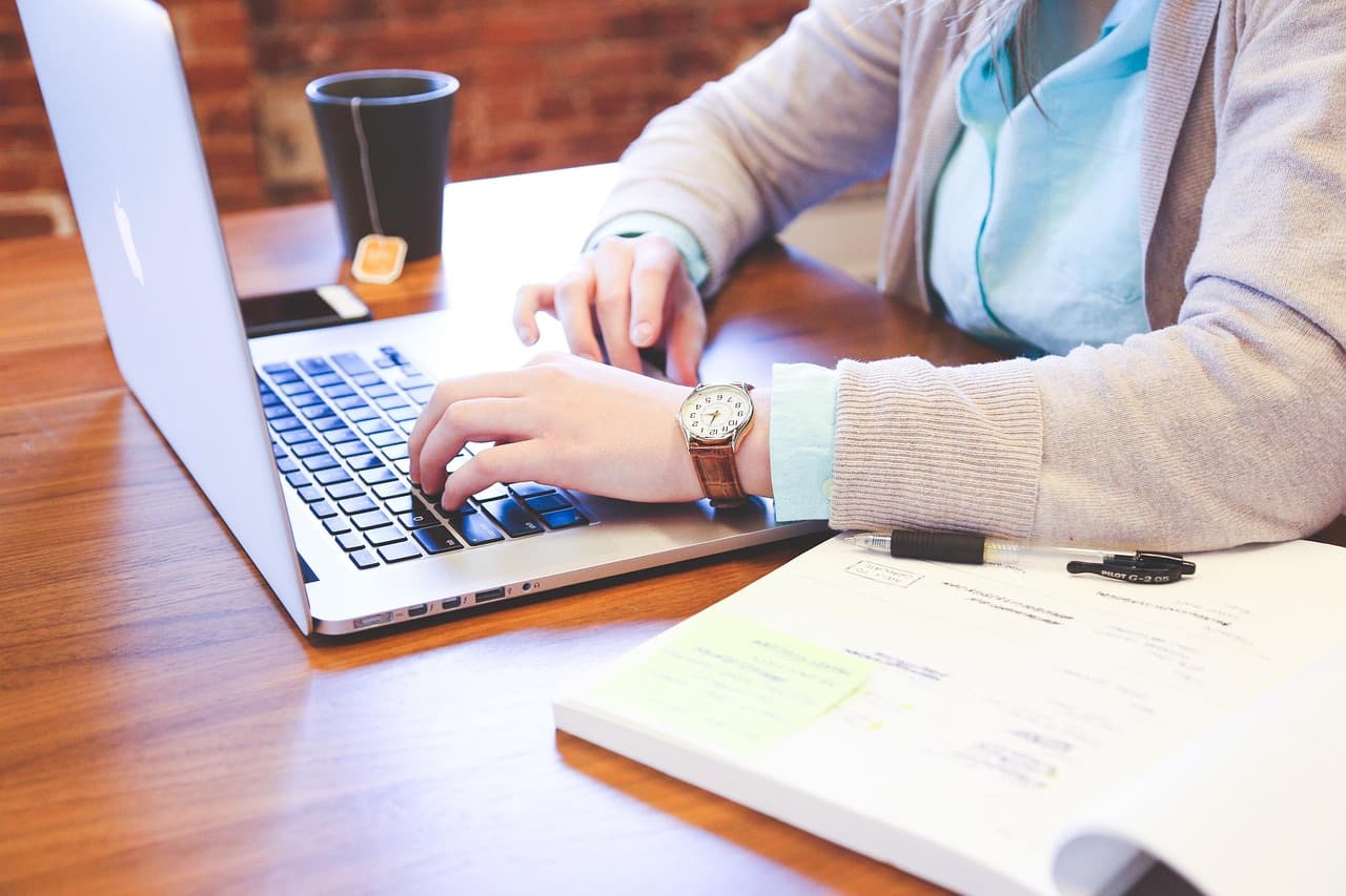 A person typing on a laptop keyboard while drafting and editing