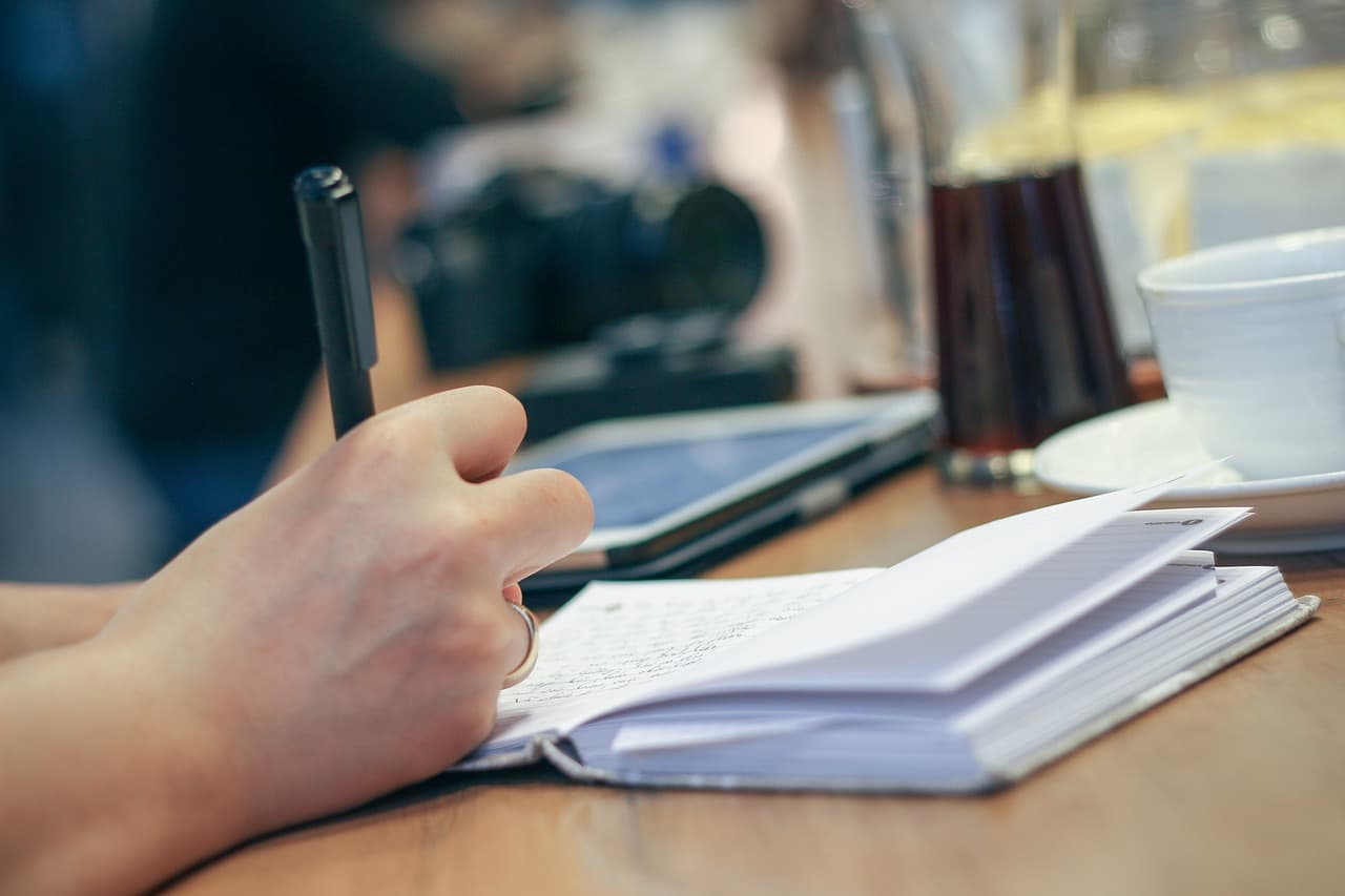 A person writing in a journal by hand, a private and specific act of putting thought into words